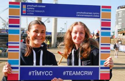 Two young adults hold up a large empty picture frame that frames their faces