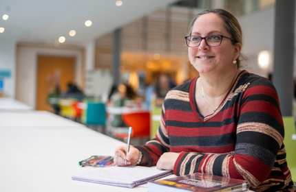 Emma Sanders looks up from writing on a notepad while sat at a desk