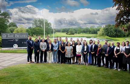 A large group of adults stand outside in front of a golf course
