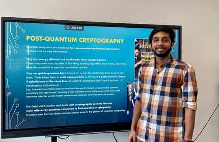 Jagan Jijo, wearing a checked shirt, stands in front of a large television screen as part of a presentation