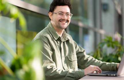 Jake Stacey sits outside on a bench working on a laptop