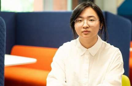 Headshot of Jiayin Bai, who is sat in front of a blue and orange study booth