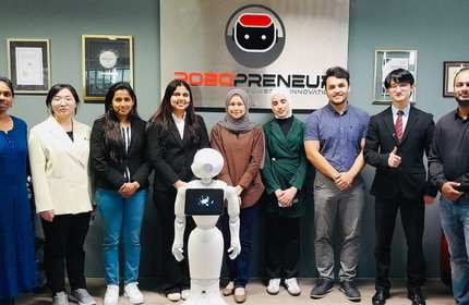 A group of individuals stand for a photograph behind a humanoid robot