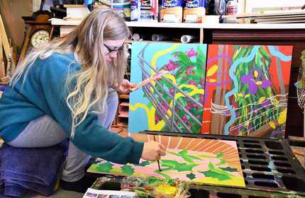 Lauren Marshall sits on a low tool and painting on a canvas that is on the floor