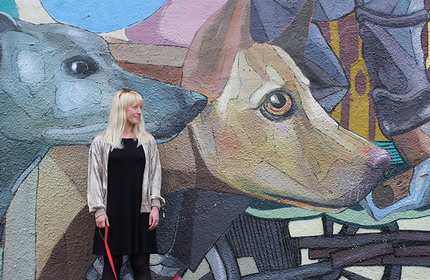 Lisa Derrick stands in front of a colourful mural featuring two dogs