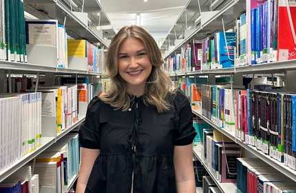 Lois Campbell stands in between two bookshelves at the library
