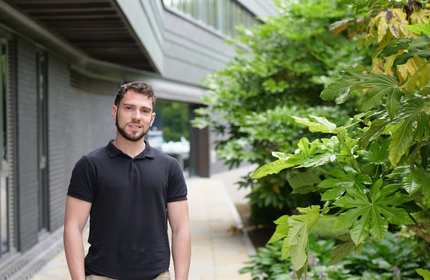 Manuele Carini stands outside the side of the Cardiff School of Management, next to some green shrubbery