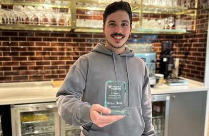 Man in grey hoodie holds an award while standing behind a drinks bar