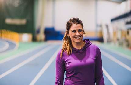 Mollie Martin stands on a blue running track at an indoor athletics centre