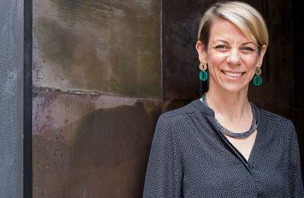 Naomi Coleman, wearing a navy polka dot top, stands in front of a stone-paved building