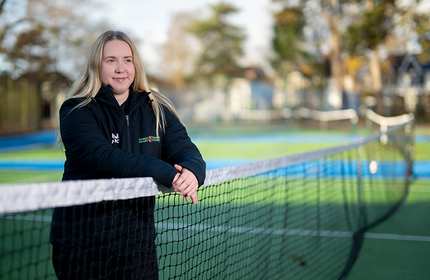 Rebecca Hannibal leans on a tennis net on a court
