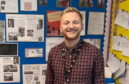 Sean Howe stands in a classroom in front of a display of history works by pupils