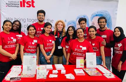 A group of individuals wearing 'I heart food science' t-shirts stand behind a display table
