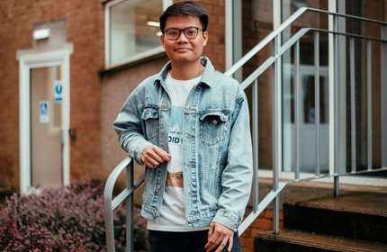 Son Tung Bui stands outside a brick and glass windowed building, leaning on the staircase railing