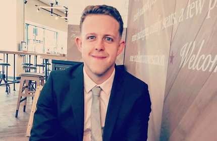 Stephen Jones sits for a photograph in an empty cafe with a branded wall on his right