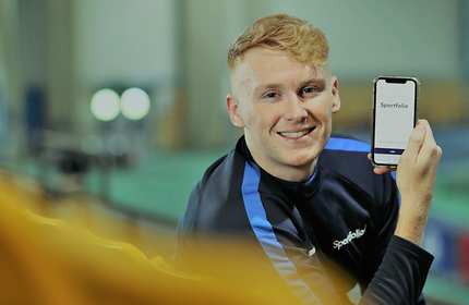 Tim Parker sits holding a mobile phone towards the camera