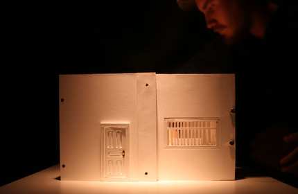 A house wall made of card on display under a dimly lit overhead light