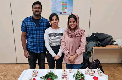 Three individuals stand behind a display table containing dessert foods and bundles of roses