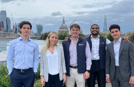 A group of young adults stand together for a photograph with the London city skyline in the background
