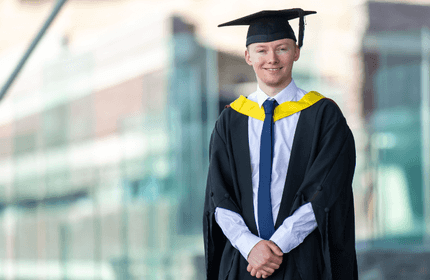 A man wearing a graduation gown and cap, celebrating his academic achievement with a proud smile.