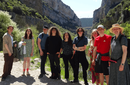 A group of people standing on a mountain trail, surrounded by lush greenery and rocky terrain.