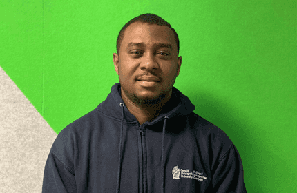 A man in a blue sweatshirt poses against a bright green wall, creating a striking visual contrast.