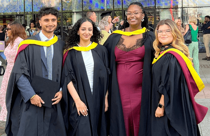 Four Cardiff Met graduates, wearing the graduation gowns, stand outside the Wales Millennium Centre
