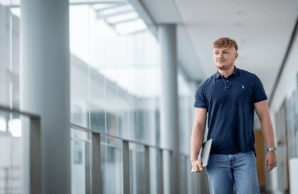 A young person walks down a mezzanine holding a laptop in one arm