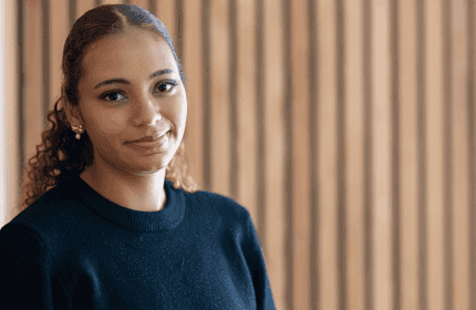 A young person in a navy jumper photographed in front of a wood panel wall