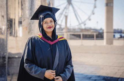 A young woman in graduate cap and gown stands for a photograph in Cardiff Bay