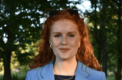 Headshot of a young woman in a blue blazer standing in front of trees and greenery