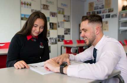 Sion Davies leans down on a table to help a pupil with their work