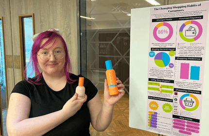 A young woman holds two small beauty products in front of an informative display