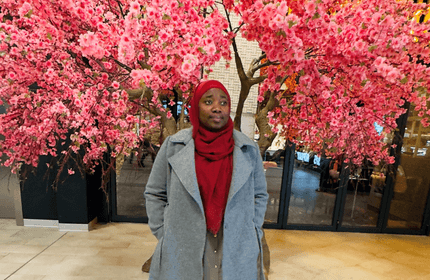 A woman wearing a red scarf stands in front of a tree, showcasing a serene outdoor setting.