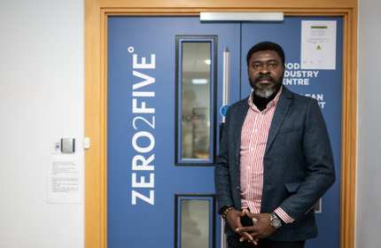 A person stands in front of a blue door. On the door is a sign that says ZERO2FIVE.