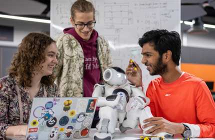 A group of people gathered around a small humanoid robot. One person is holding a screwdriver in their hand.