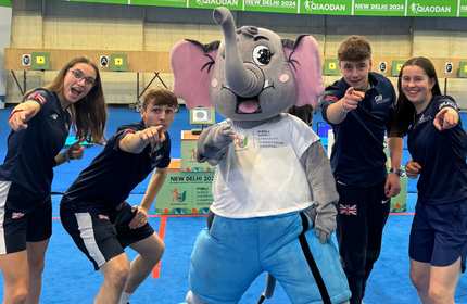 Four young people wearing sport clothing point at the camera. Standing between them is a person dressed in an elephant costume.