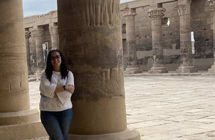 A person stands next to an old stone column. In the background is row of columns and a high stone wall.
