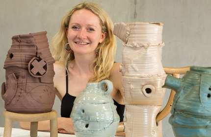 A person sits at a table. Arranged in front of them are four ceramic vases in a variety of colours.
