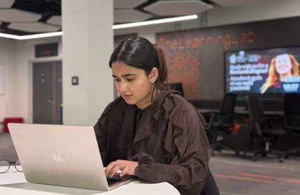 A person sits a round table, working intently at a laptop computer.
