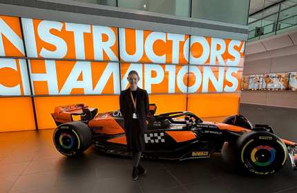 A person stands in front of a Formula 1 car inside a modern building.