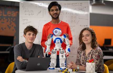 A person steadies a small humanoid robot that is standing on round table.