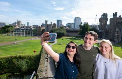 A group of three people taking a selfie with a castle and city skyline in the background.