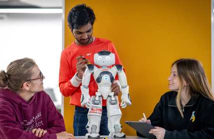 A person makes an adjustment to a small humanoid robot while two other people look on.