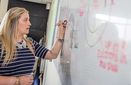 Teacher writes on a whiteboard with a red marker pen.