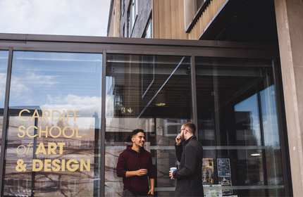 Two students talk outside the glass entrance to the Cardiff School of Art and Design