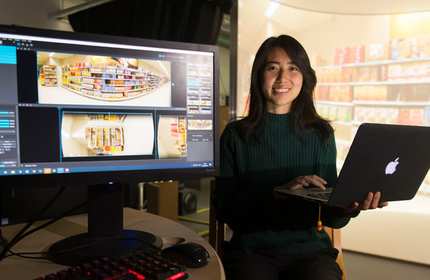 Member of staff holds laptop and stands in front of large computer monitor