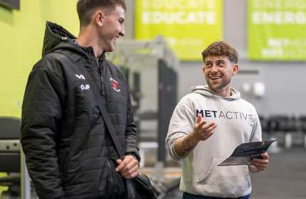 Two men wearing gym gear chatting in the gym, and one has a great hoodie on with Met Active on it.