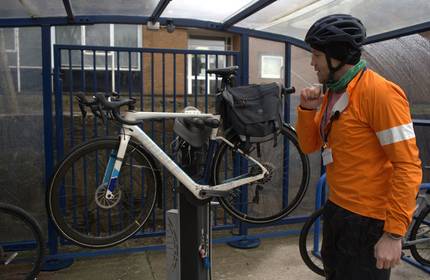 A man in high visibility clothing inspects his bicycle on a lifted stand
