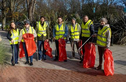 A group of litter pickers in high visibility vests hold waste bags and litter picking sticks
